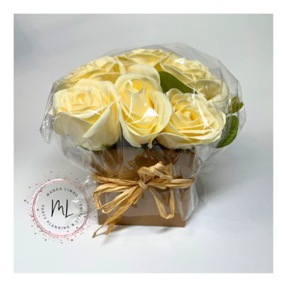 Arranjo de flores artificiais amarelo claro em caixa de papel com laço e plástico transparente.