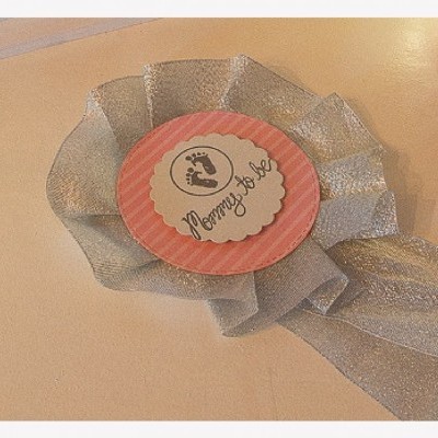 Medalha para recém-nascido com fita prateada e círculo rosa com pegadas e texto