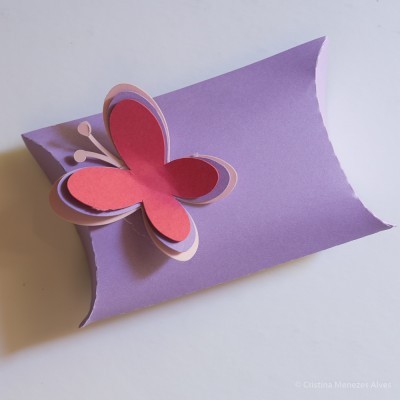 Caixa almofada lilás com borboleta de papel rosa e vermelho em cima