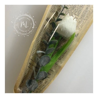 Flor branca artificial embrulhada em papel estilo jornal com folhas verdes artificiais