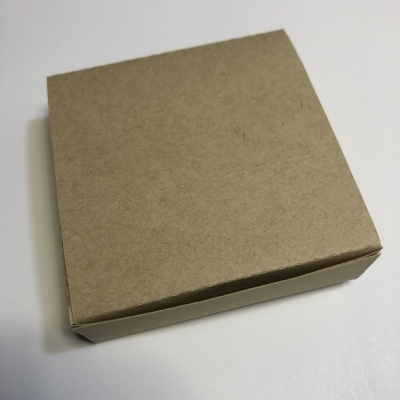 Caixa quadrada de cartão castanho claro numa superfície branca