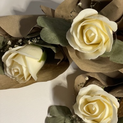 Flores artificiais com rosas creme e folhas verdes em papel castanho