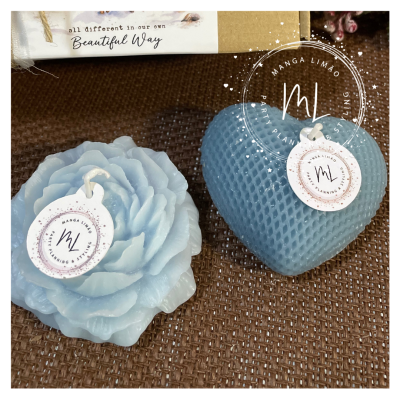 Velas decorativas azuis em formas de flor e coração com etiquetas da marca Manga Limão sobre superfície castanha texturizada