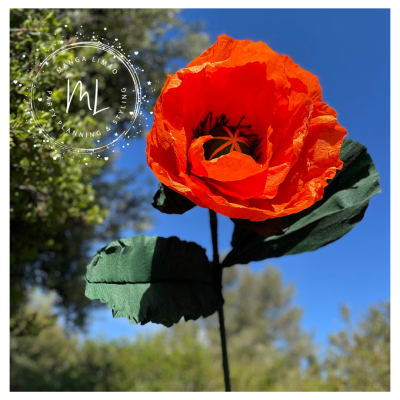 Flor artificial de papel alaranjada com folhas verdes e fundo de céu azul