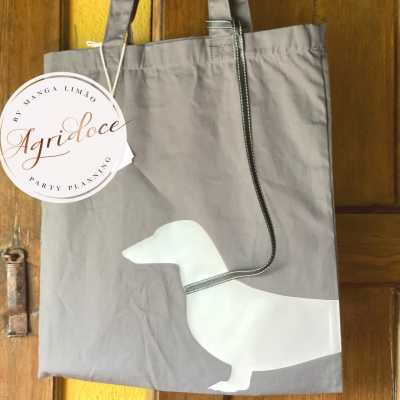 Saco cinzento com impressão branca de cão dachshund pendurado numa porta de madeira