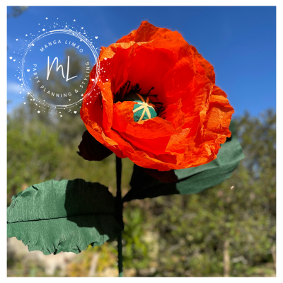 Flor artificial vermelha de papel com folhas verdes e fundo de vegetação