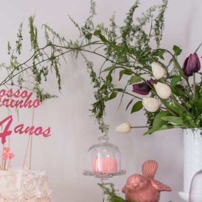 Bolo de aniversário com decoração e flores em jarra branca numa mesa clara