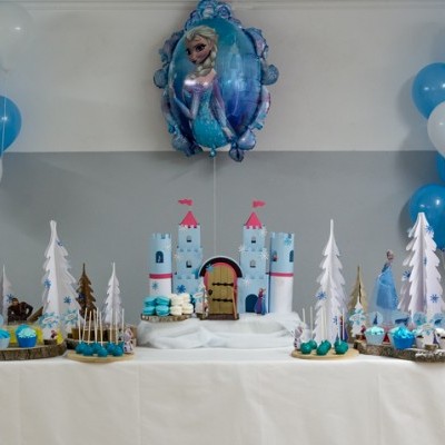Mesa de festa infantil com decoração azul e branca, bolo de castelo e balões.