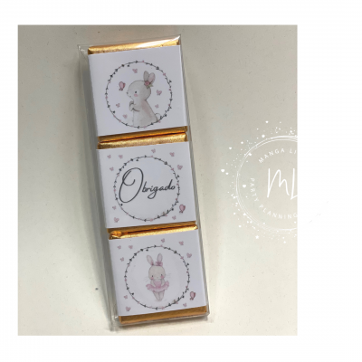 Três chocolates pequenos com embalagens brancas e douradas, decoradas com desenhos de rato, coelho e a palavra 'Obrigado' cercados por flores, em embalagem plástica.