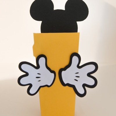 Caixa amarela com recorte da cabeça do Mickey Mouse e mãos brancas decorativas