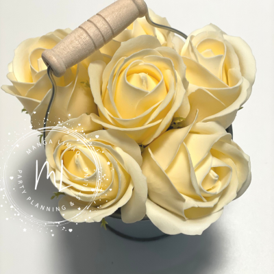 Flores artificiais creme em balde metálico com alça de madeira.