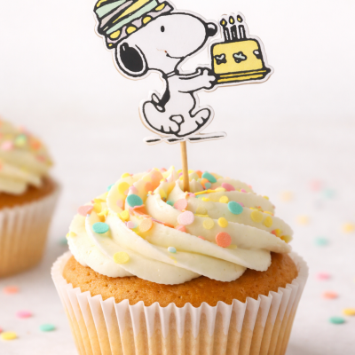 Cupcake com cobertura branca, confeitos coloridos e topper do Snoopy com bolo amarelo