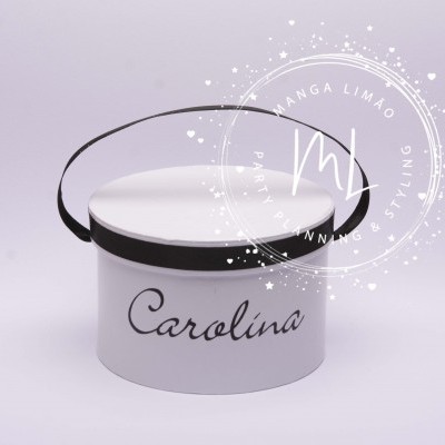 Caixa redonda branca com fita preta, com o nome Carolina em letra cursiva.