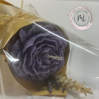 Vela roxa em forma de flor embalada em plástico com ramos secos decorativos