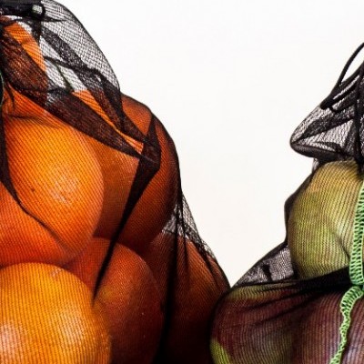 Sacos de malha preto com laranjas e pêras verdes num fundo branco