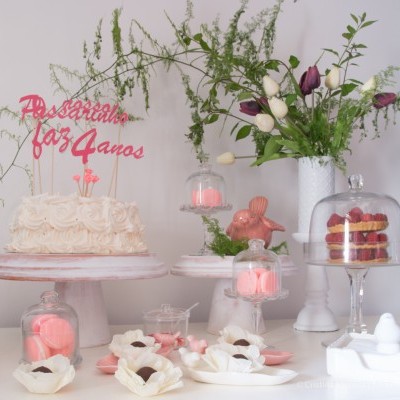 Bolo branco com decoração de texto 'Passarinho faz 4 anos', flores e doces em mesa decorada.