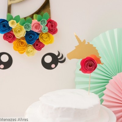 Bolo branco com decoração de unicórnio e flores de papel coloridas na parede