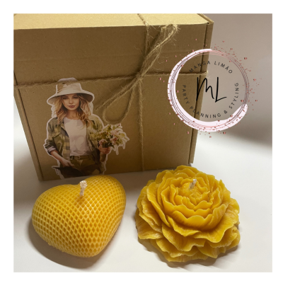 Conjunto de duas velas amarelas, forma de coração e flor, com caixa de papelão decorada e selo redondo.