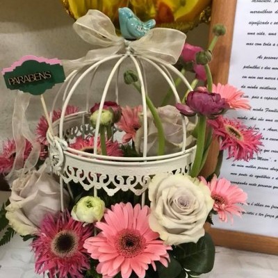 Arranjo floral em gaiola branca com flores rosa e brancas e etiqueta PARABENS