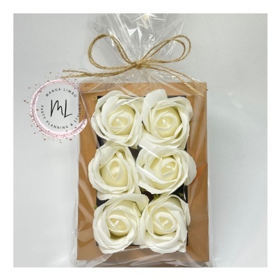 Seis rosas brancas artificiais em embalagem plástica com laço de corda e selo redondo ao lado.