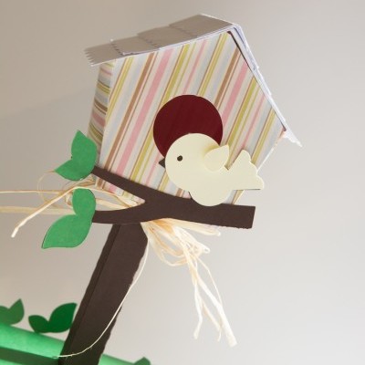 Casa de passarinhos em papel com padrão às riscas, pássaro amarelo e folhas verdes