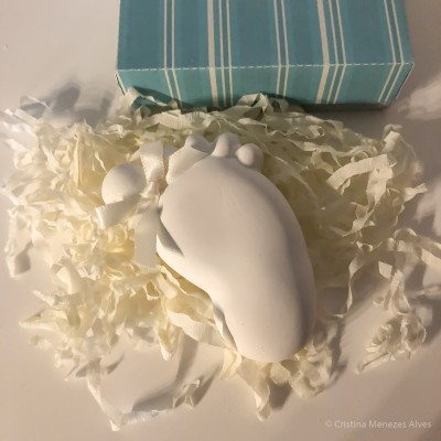 Escultura branca de pé de bebé com caixa azul riscada e papel de embrulho