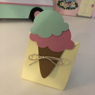 Caixa de papel amarelo com decoração de gelado colorido e cordão amarrado