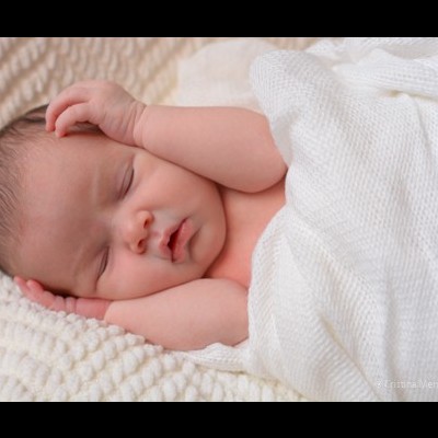 Bebé recém-nascido adormecido envolto em cobertor branco num tecido macio
