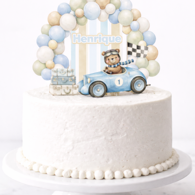 Bolo branco com decoração de ursinho num carro azul com o nome Henrique e balões coloridos