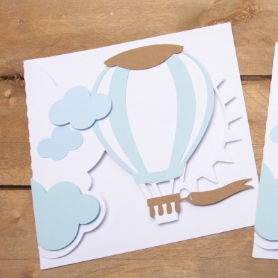 Cartão com balão de ar quente e nuvens em papel azul e castanho sobre fundo de madeira