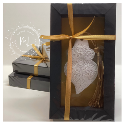 Caixas presentes pretas com laços dourados e um ornamento pendente branco em forma de coração com franja dourada dentro de uma caixa maior.
