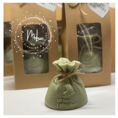 Pequeno saco decorativo verde claro com texto Merry Christmas e desenho de patins, colocado numa mesa com embalagens castanhas com velas dentro