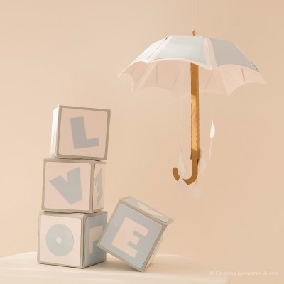 Cubos com letras formando LOVE ao lado de guarda-chuva branco suspenso num fundo castanho claro