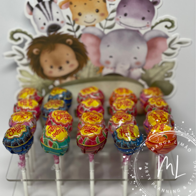 Pirulitos Chupa Chups coloridos em expositor com fundo decorativo de animais desenhados.