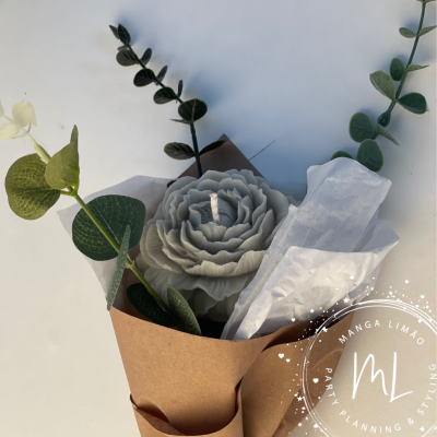 Vela em forma de flor cinzenta com folhas verdes, embrulhada em papel castanho e branco com selo MANGA LIMÃO.