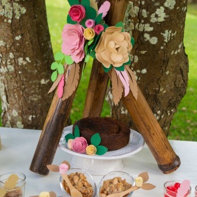 Bolo decorado com flores de papel e copos com granola em mesa ao ar livre