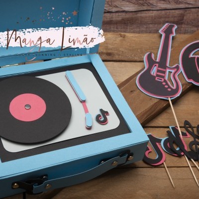 Caixa azul em formato de gira-discos com disco preto e recortes de papel de guitarra e notas musicais sobre madeira