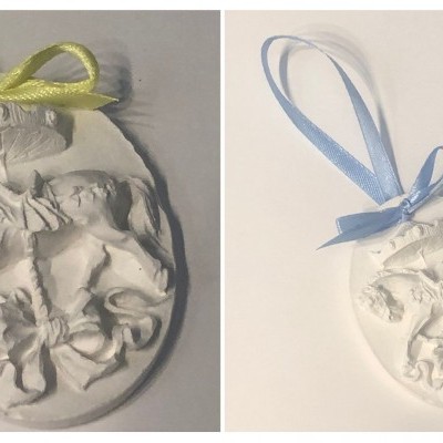 Medalhões ovais brancos com relevo de anjos e fitas verde e azul.