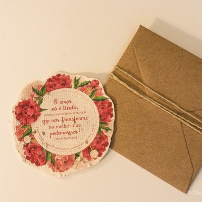 cartão floral redondo com texto em português e envelope castanho amarrado com cordão