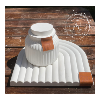 Frascos brancos de cerâmica com tampa e detalhes em couro sobre placa branca ondulada numa mesa de madeira.