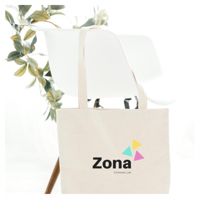 Saco de tecido bege com logotipo pendurado numa cadeira branca com pernas de madeira