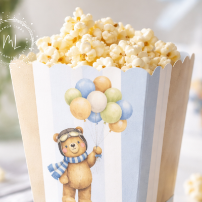 Saco decorativo com ursinho e balões cheio de pipocas sobre mesa clara