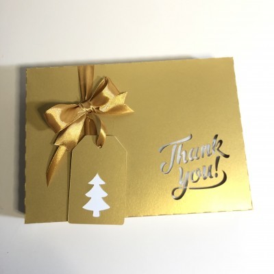 Caixa dourada com laço dourado e etiqueta com árvore branca e 'Thank you!' em relevo