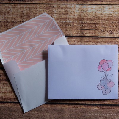 Envelope branco com padrão rosa no interior e cartão com elefante e balões cor de rosa