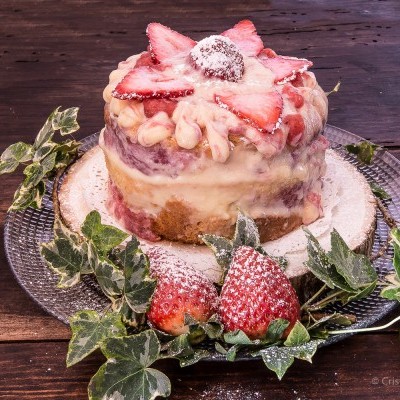 bolo pequeno decorado com creme, morangos e folhas verdes sobre prato de vidro