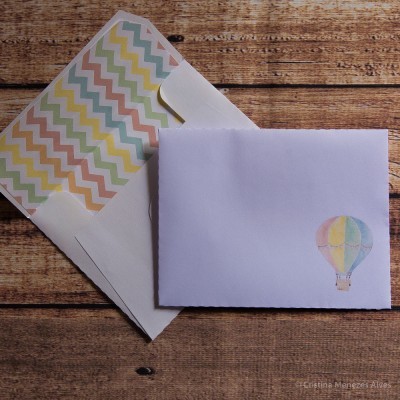 Dois envelopes sobre mesa de madeira, um com padrão colorido interior e outro fechado com ilustração de balão