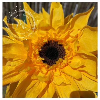 Flor artificial amarela tipo girassol com centro castanho escuro e fundo de madeira desfocada
