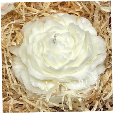 Vela branca em forma de flor rodeada por palha seca