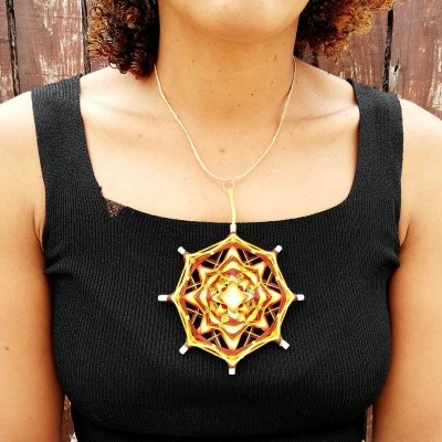 Colar pendente geométrico dourado e preto usado por mulher com camisola preta