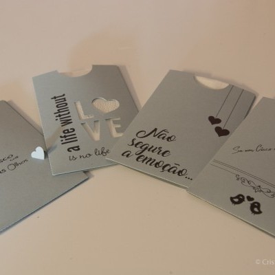 Quatro envelopes cinzentos com texto em português e inglês e detalhes de corações pretos.
